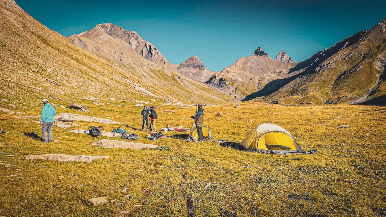A group of hikers set up tents beneath the majestic Aiguilles d'Arves.