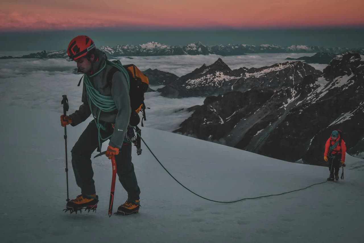 Mountaineers climbing a glacier on Mont Rose, with a brilliant sunrise in the background.