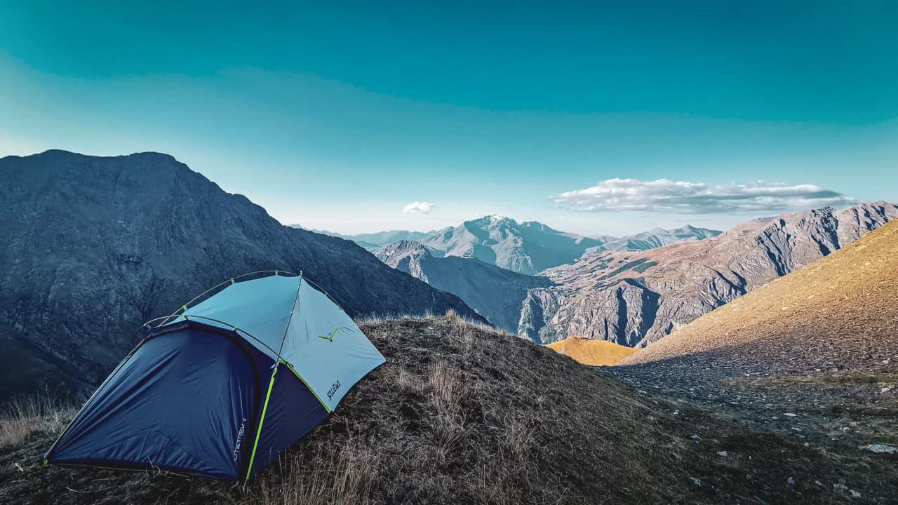 Colourful tent on a steep summit with spectacular views of the surrounding mountains.