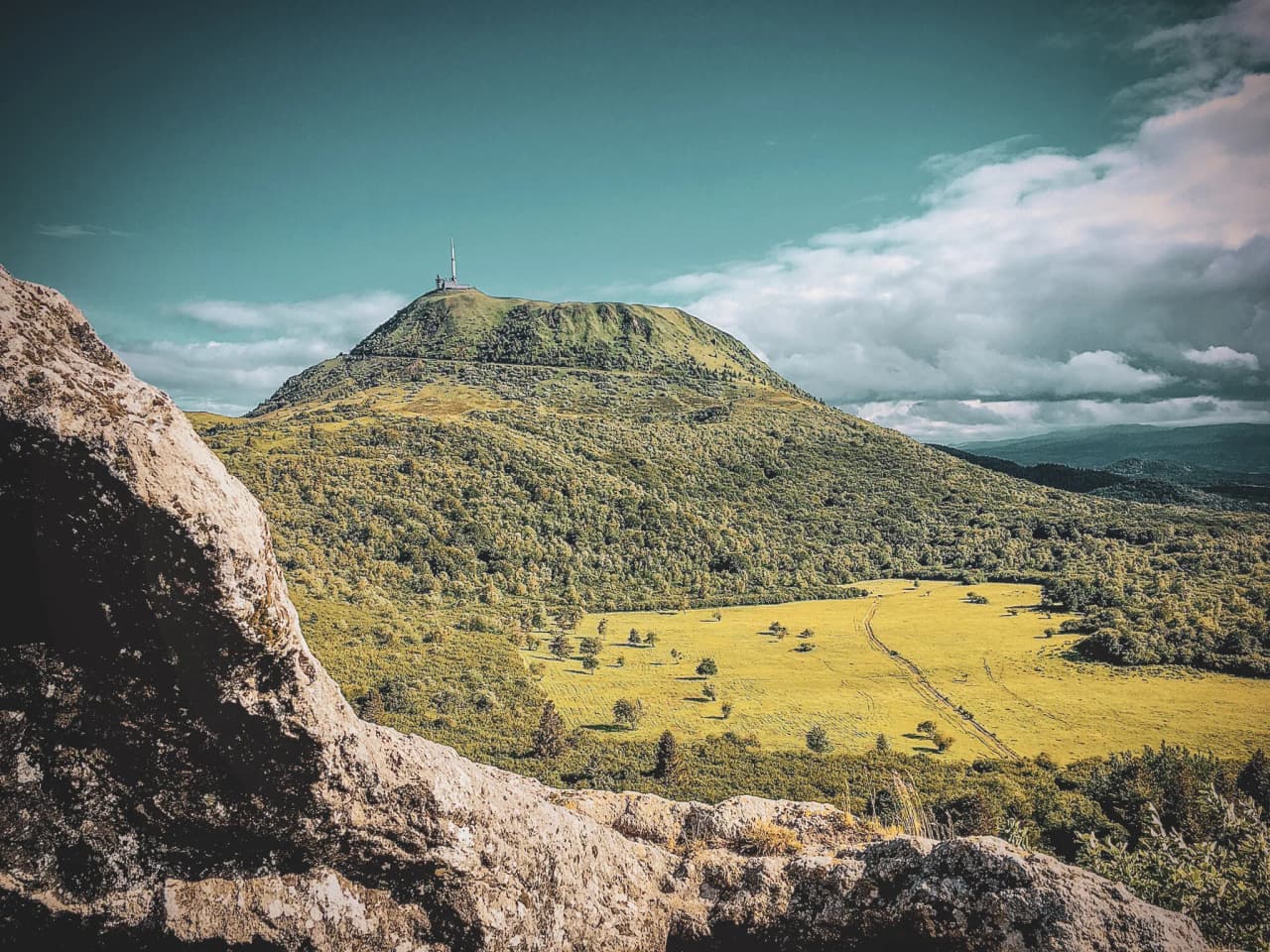 A green panorama of the Massif Central, with the Puy de Dôme towering under a luminous sky.