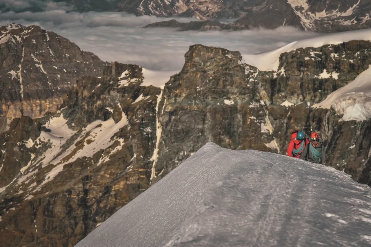 Mountaineers on a snow-capped peak, with majestic mountains in the background.