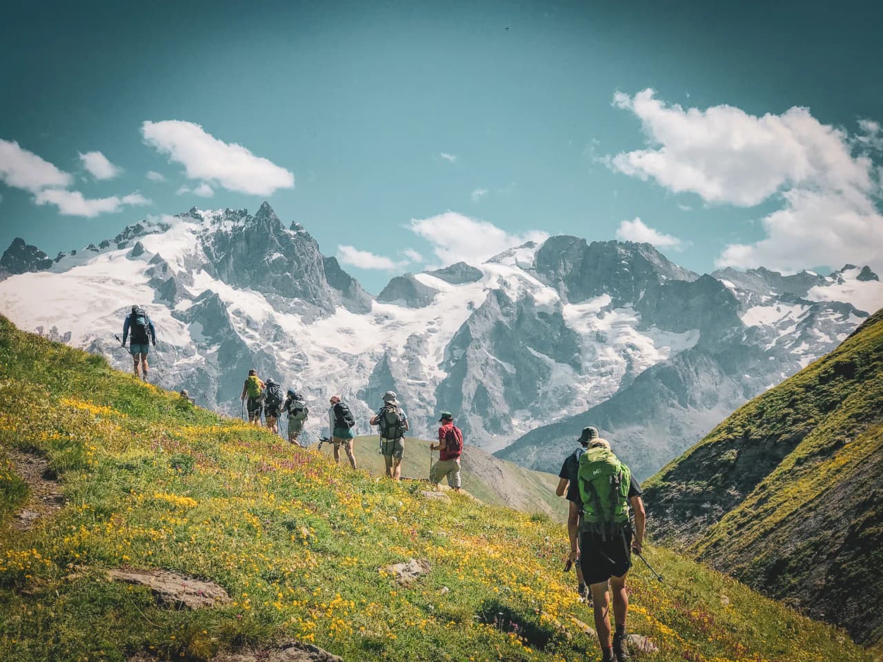 Hikers on a flower-filled trail, surrounded by majestic mountains with eternal snow.