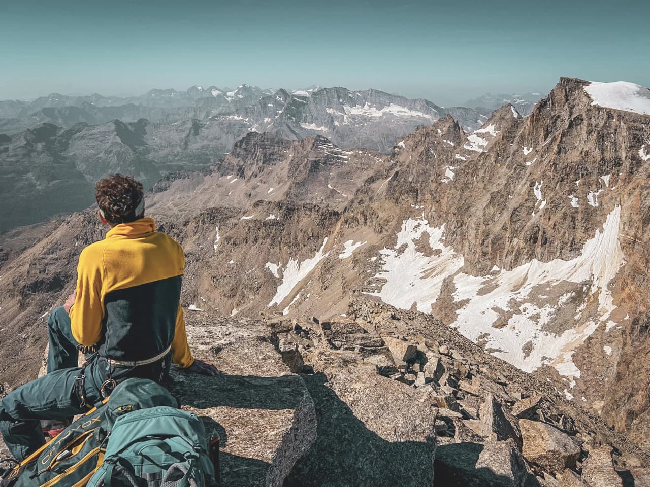 A mountaineer contemplating the majestic peaks of Gran Paradiso, on a sun-drenched rock face.