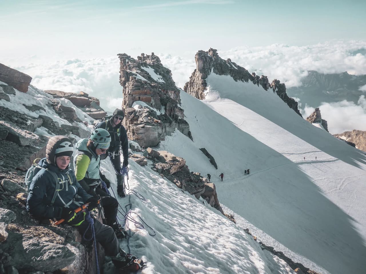 Mountaineers on a snow-covered summit, with wispy clouds and majestic peaks in the background.