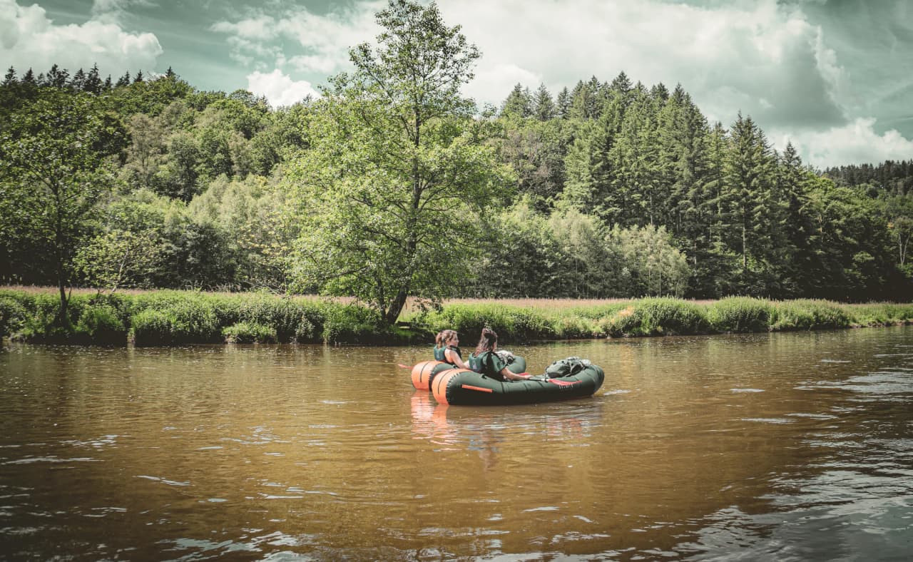 Peaceful packraft hikers on the Semois, surrounded by lush green countryside.