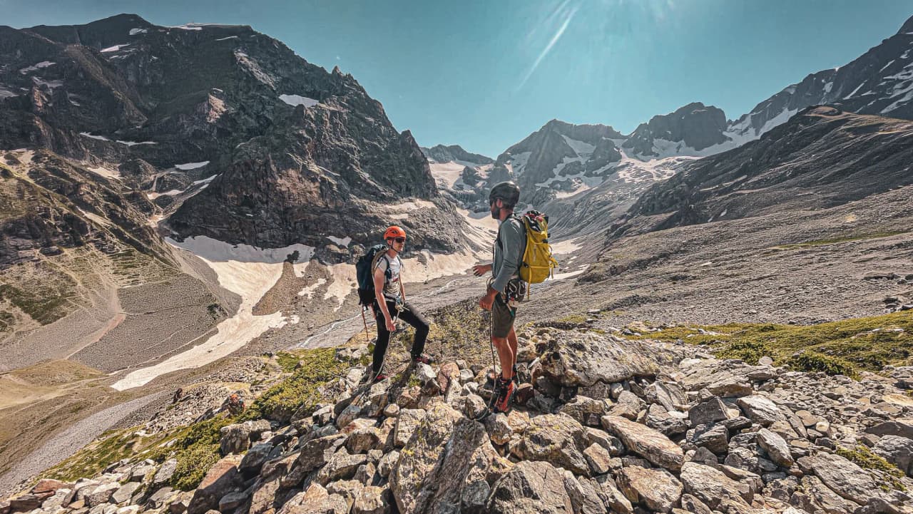 Two climbers chat among the rocks, with the majestic Écrins mountains in the background.