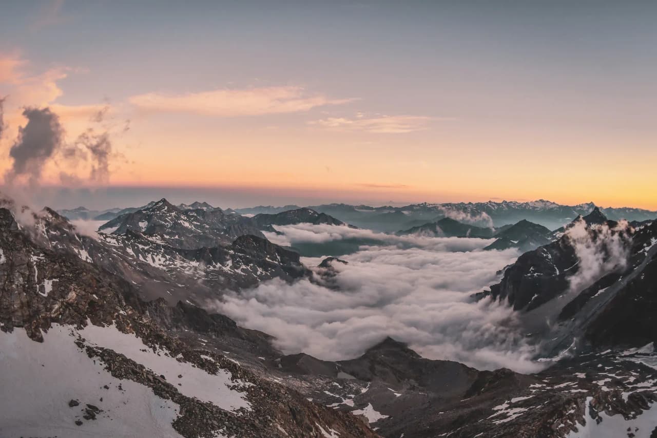 A majestic sunrise over the peaks of the Alps, surrounded by clouds. A dream of escape.