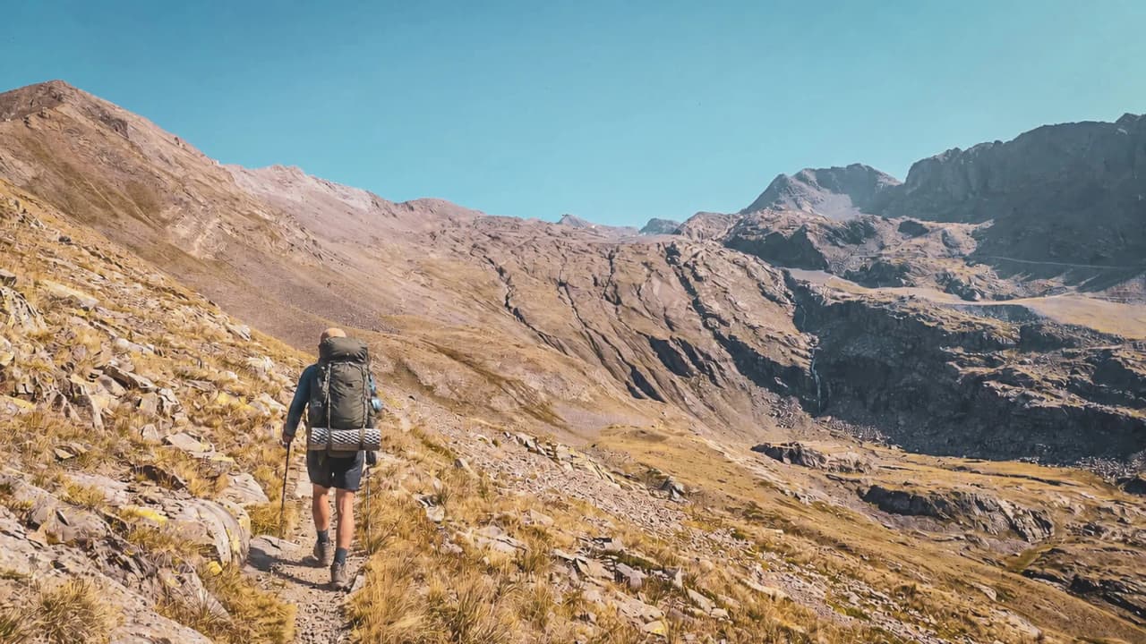 Hiker traversing an arid alpine landscape, with majestic peaks in the background.