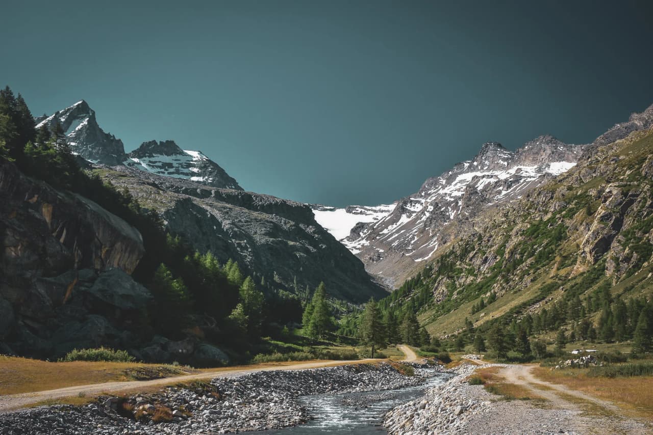 A mountainous landscape with snow-capped peaks, a lush green valley and a winding path.