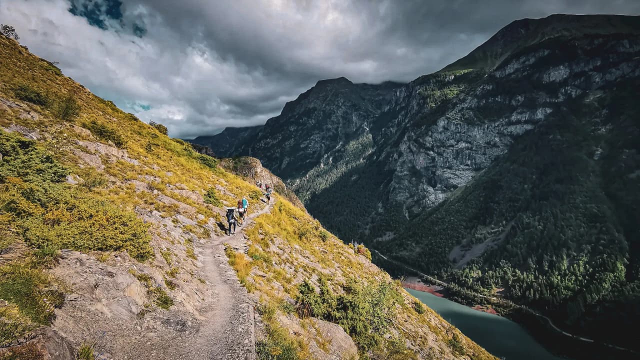 Picturesque mountain trail with hikers, views of majestic peaks and a lake.