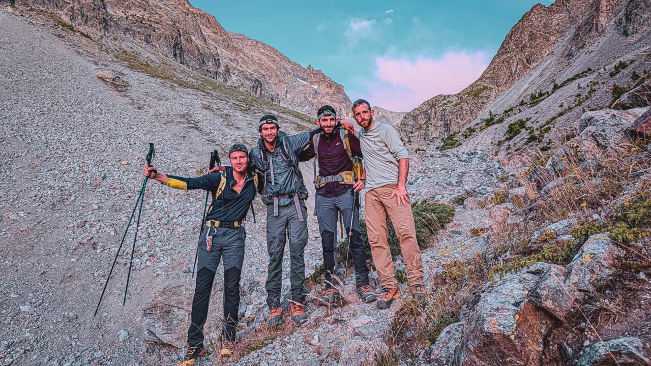 Four smiling friends pose in the middle of nature, surrounded by the majestic mountains of the Écrins.