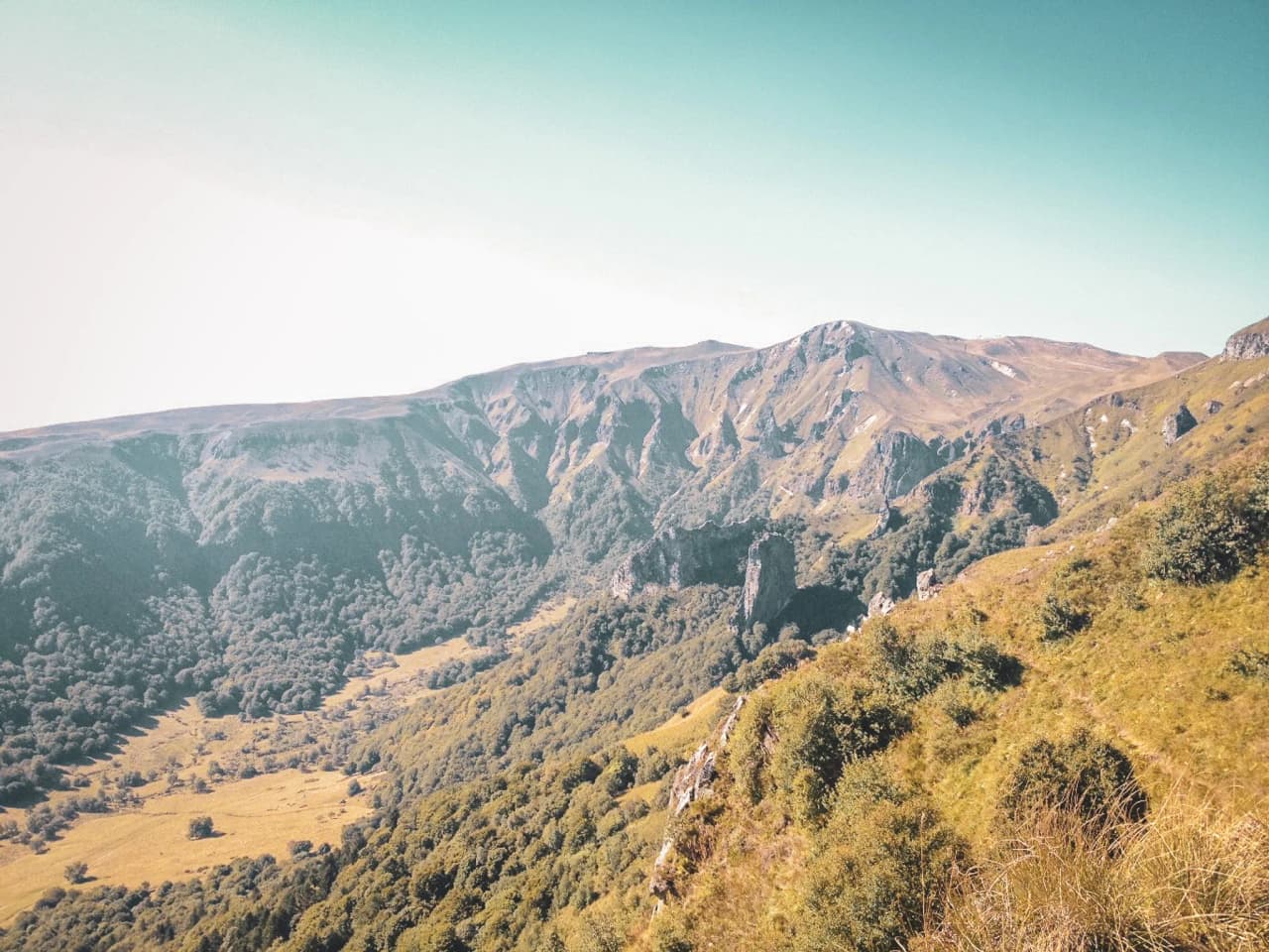 A panoramic view of the volcanic ridges of the Massif Central, surrounded by greenery and blue skies.
