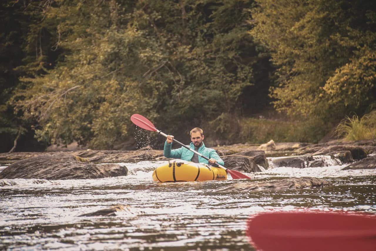 A man paddles in a tranquil river, surrounded by wild nature in the Ardennes.