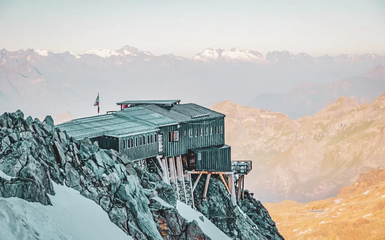 An alpine mountain hut perched on a rocky outcrop, surrounded by the majestic peaks of Mont Rose.