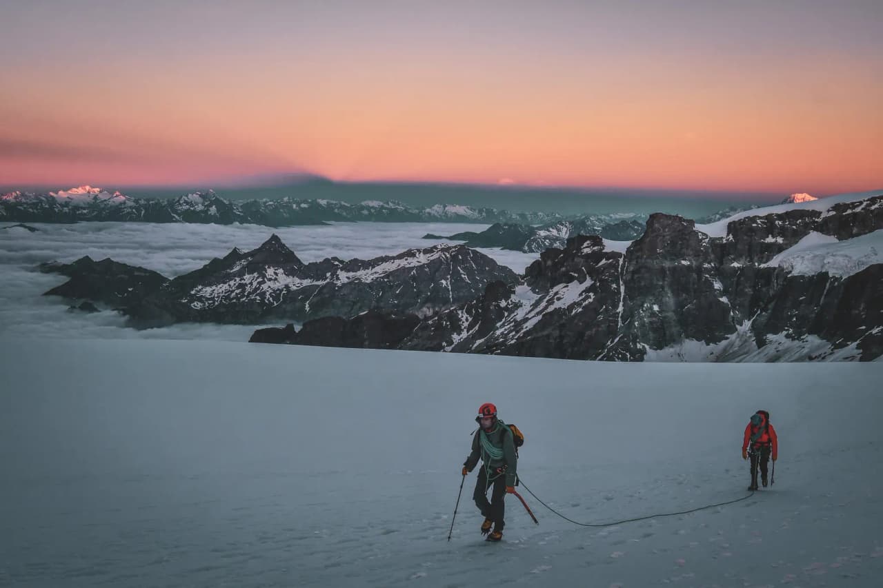 Mountaineers crossing a glacier in the early morning, facing majestic peaks.