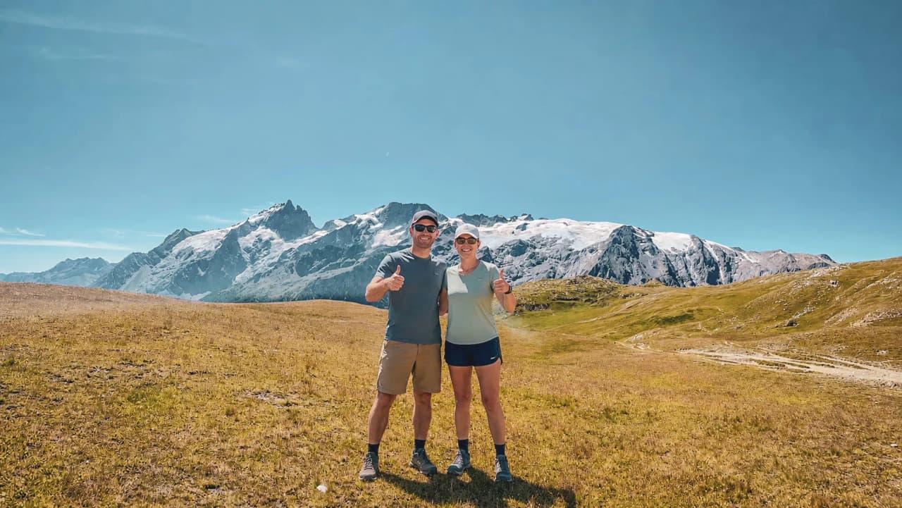 A smiling couple in the middle of nature, with majestic mountains in the background.