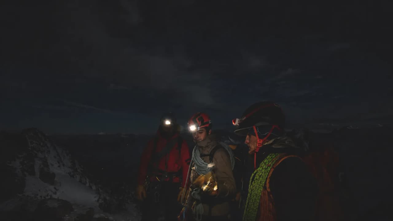 Three mountaineers equipped with headlamps, ready for a night-time adventure in the mountains.