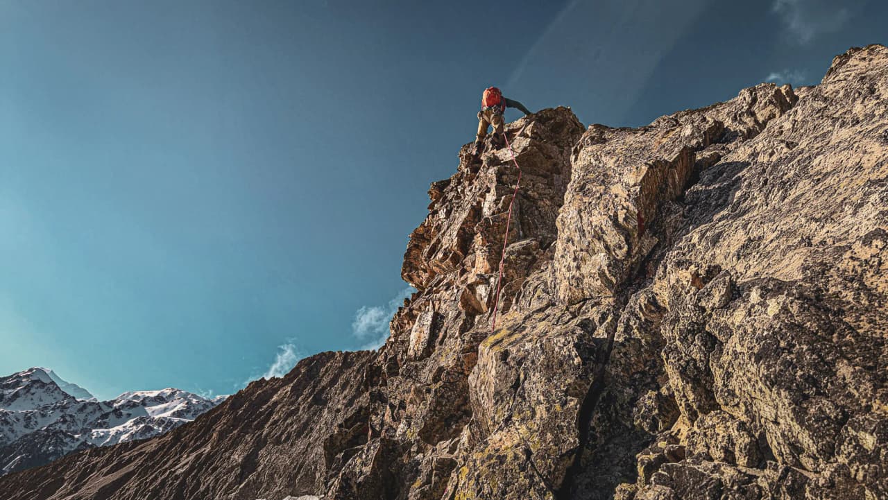 Mountaineer climbing a rock face in the Écrins under a brilliant blue sky.