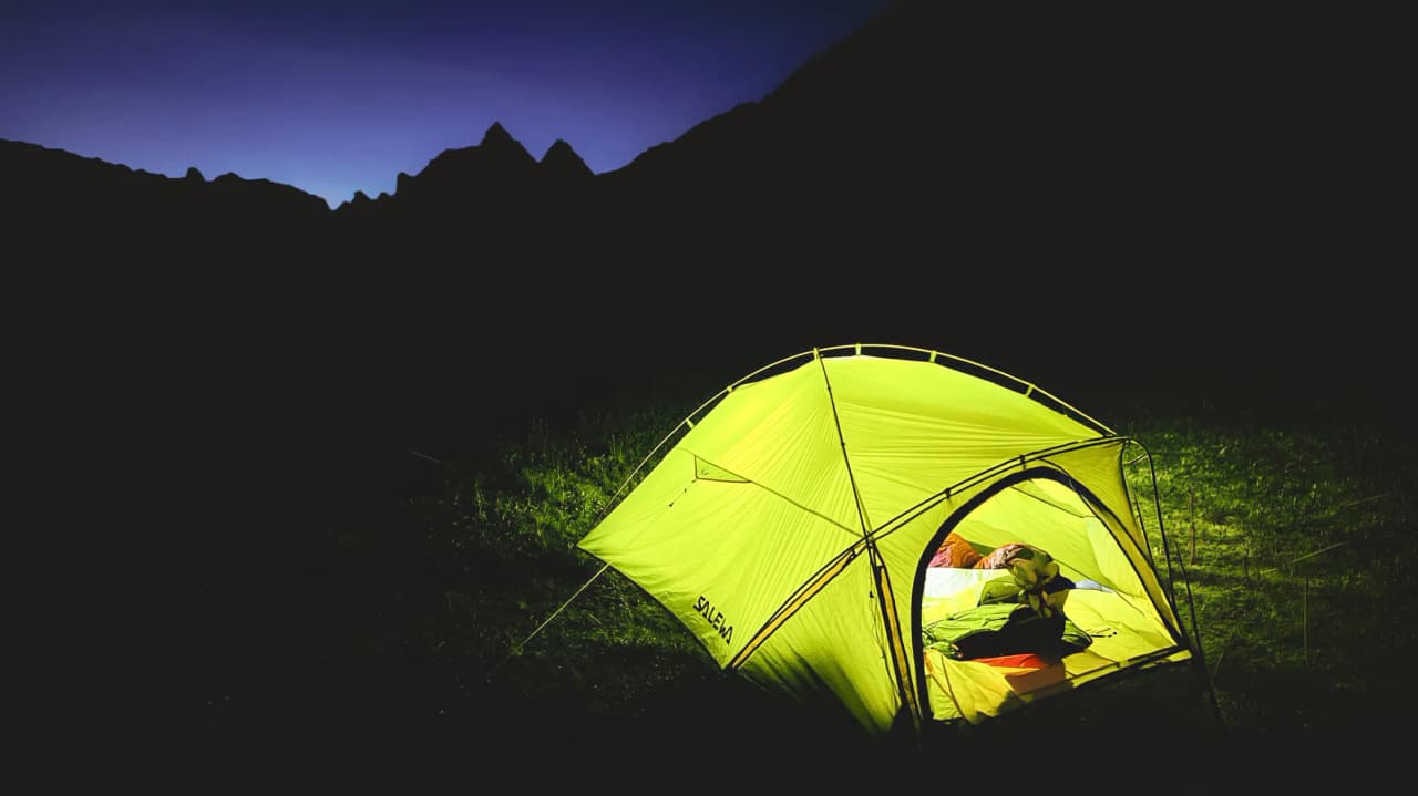 A luminous tent under a starry sky, surrounded by majestic mountains. An Alpine escape.