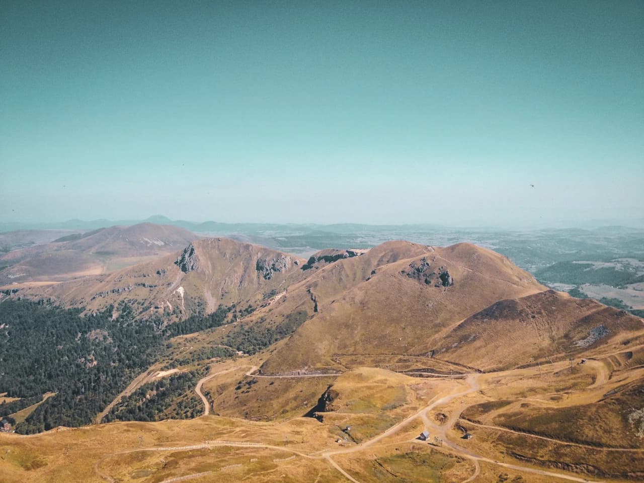 The mountain landscape of the Massif Central, with volcanic peaks and lush green valleys under a blue sky.
