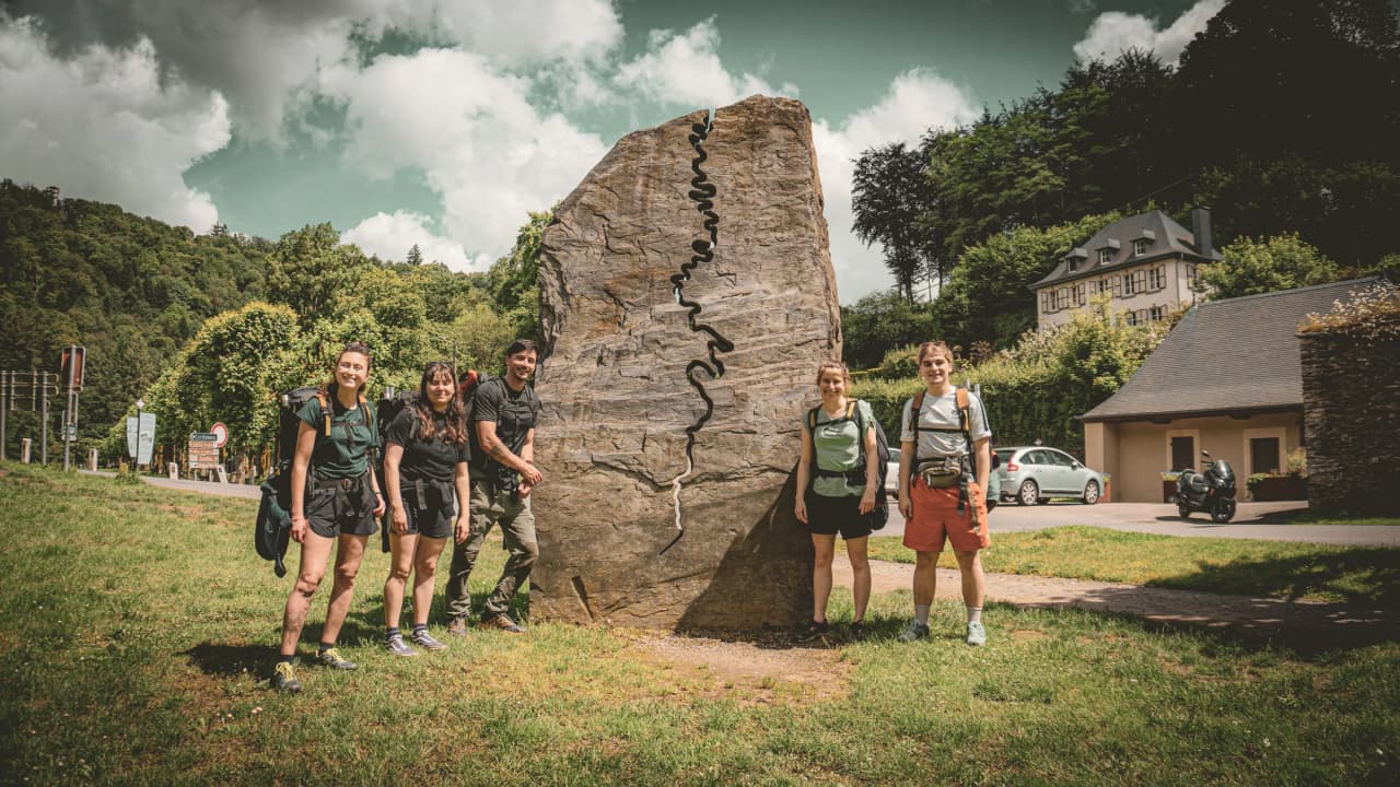 A group of smiling adventurers by a carved rock, ready to explore the Semois valley.