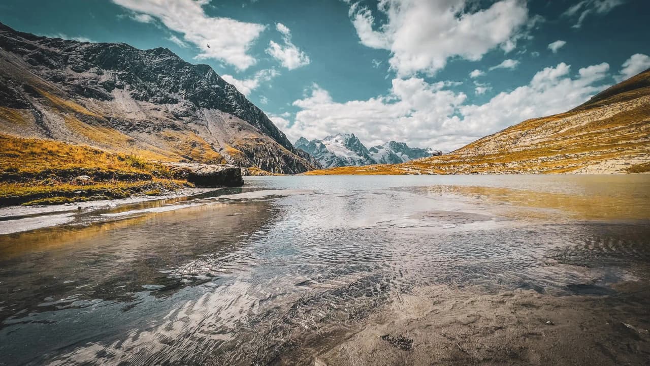 A turquoise lake surrounded by majestic mountains, blue skies dotted with clouds, an invitation to adventure.