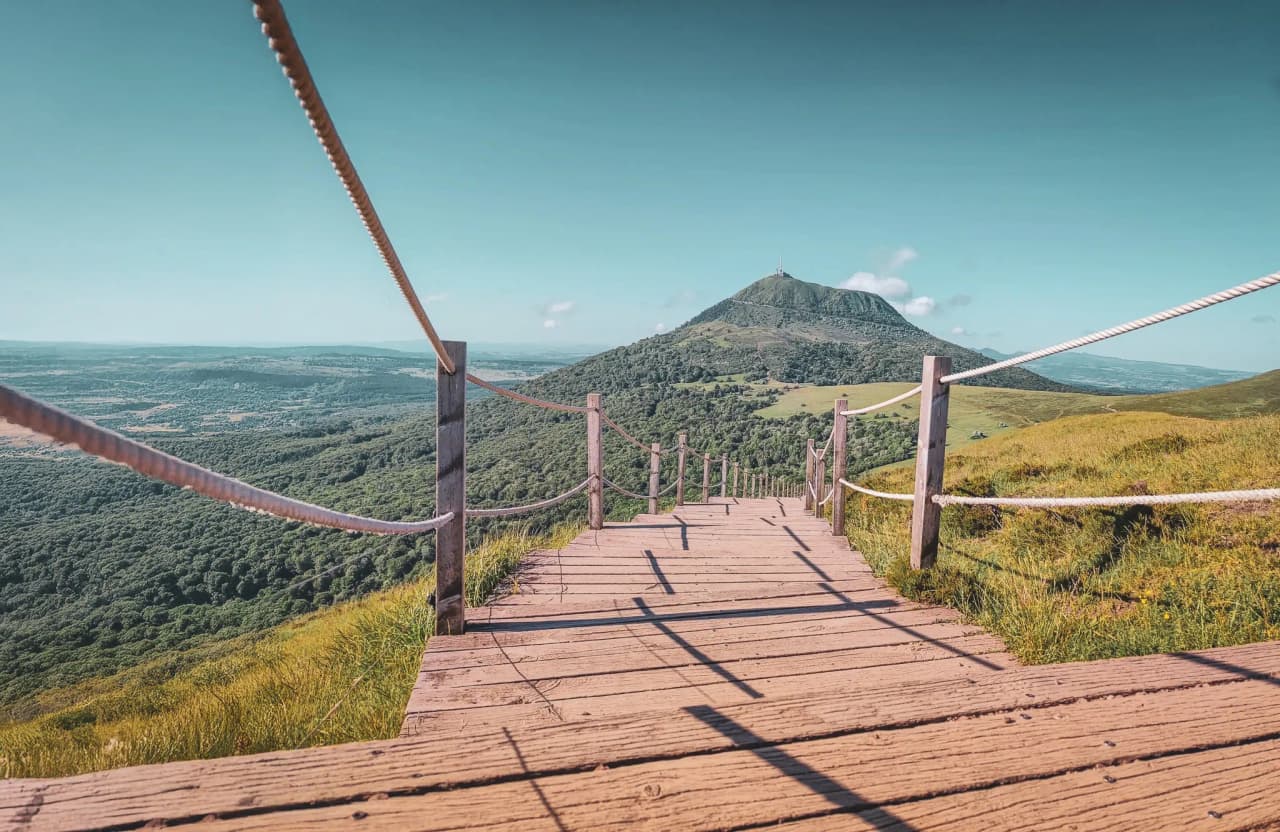 Wooden path lined with ropes, panoramic view of the green mountains of the Massif Central.