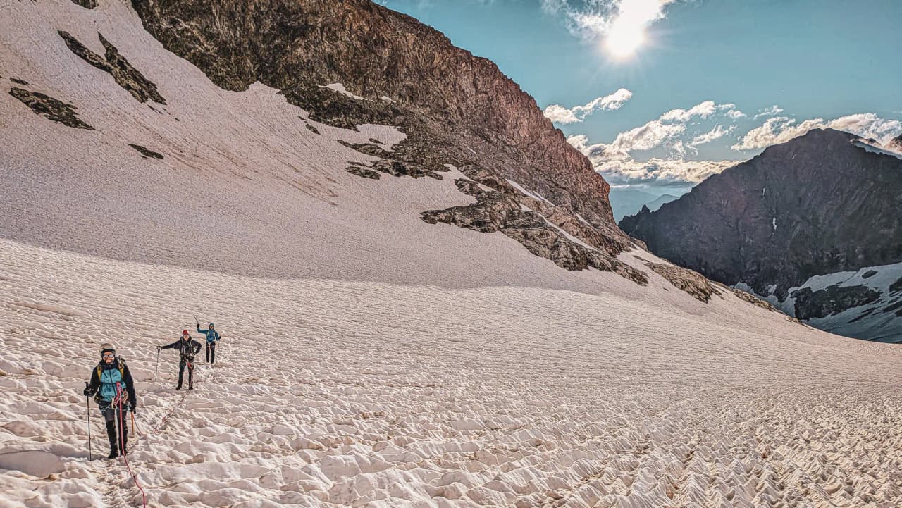 Three climbers are making progress on a glacier in the Écrins, under a majestic, sunny sky.
