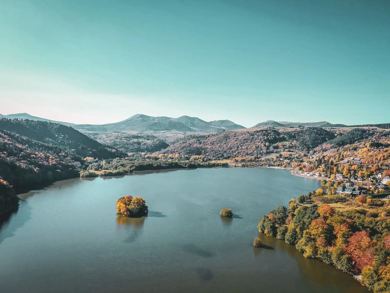 "Peaceful lake surrounded by colourful hills, inviting for walking and swimming."