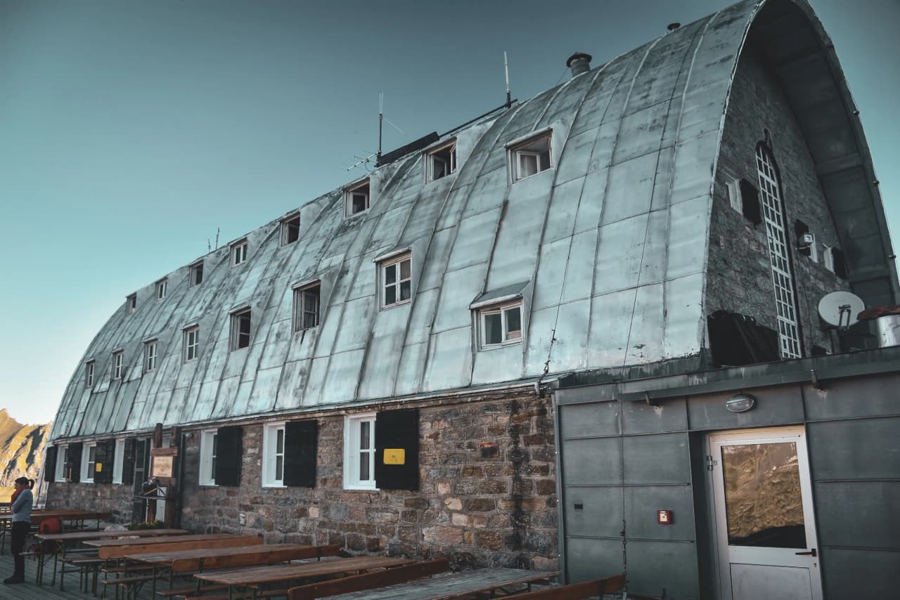 Alpine Mountain hut with a metal and stone façade, offering views of the surrounding peaks.