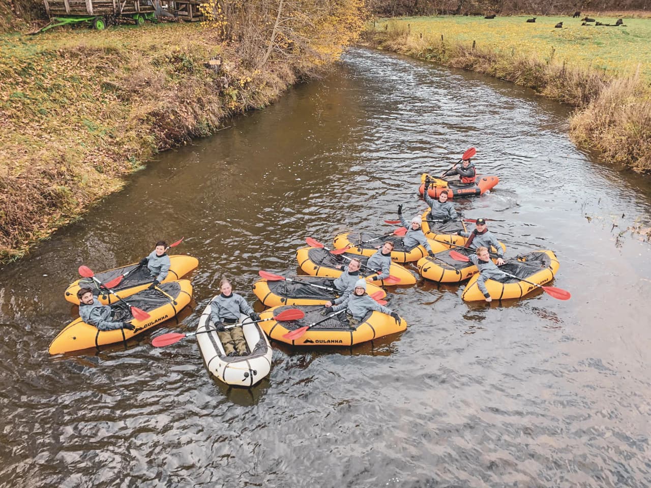 A happy group in orange packrafts on a peaceful river surrounded by nature in the Ardennes.