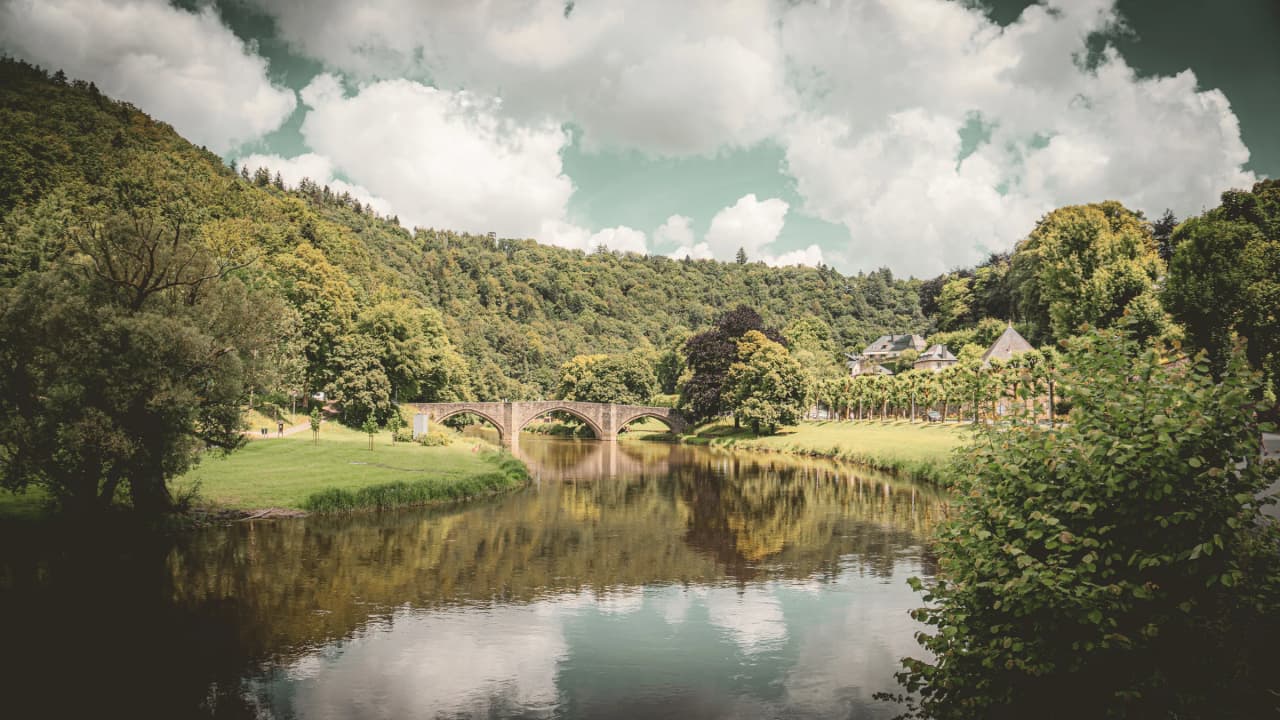 Stone bridge over the River Semois, surrounded by lush greenery and peaceful hills.