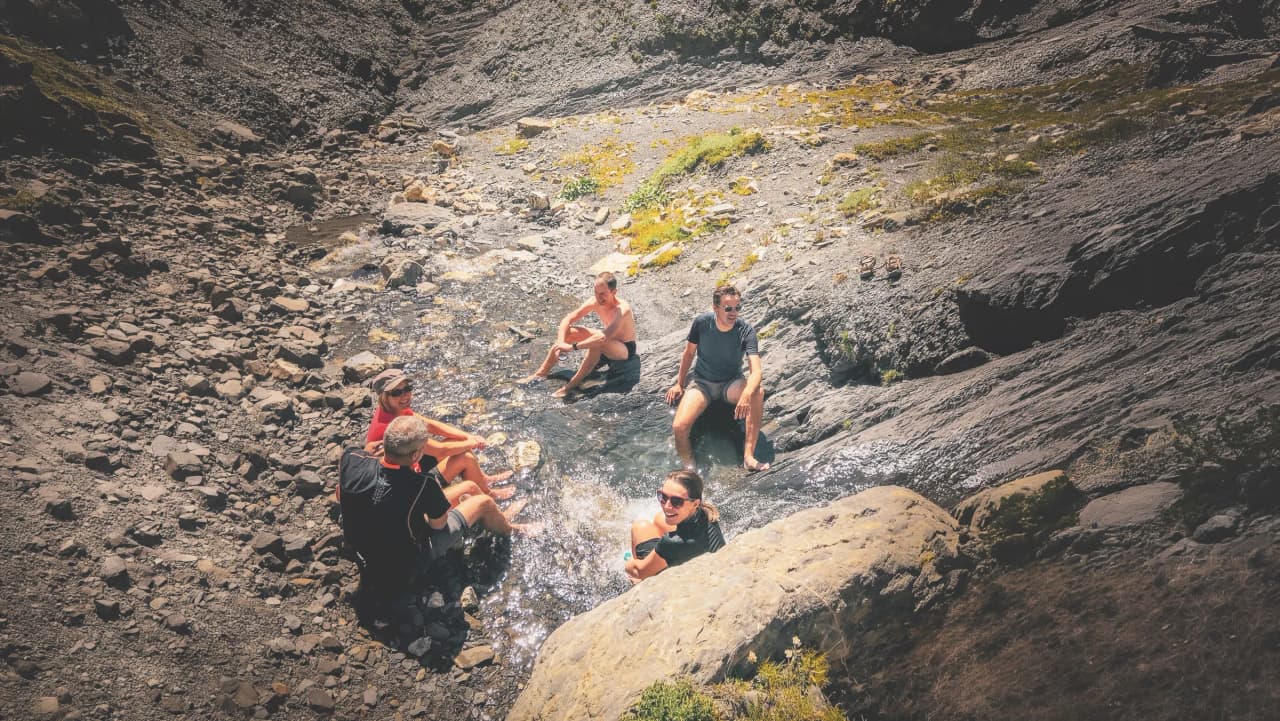 A group of friends relaxing in a mountain stream, surrounded by stones and greenery.