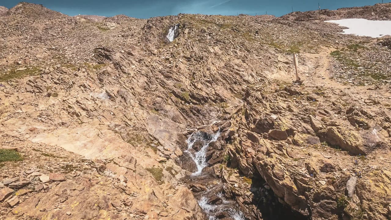 Rocky Alpine scenery with a crystal-clear stream and blue skies, an invitation to adventure.