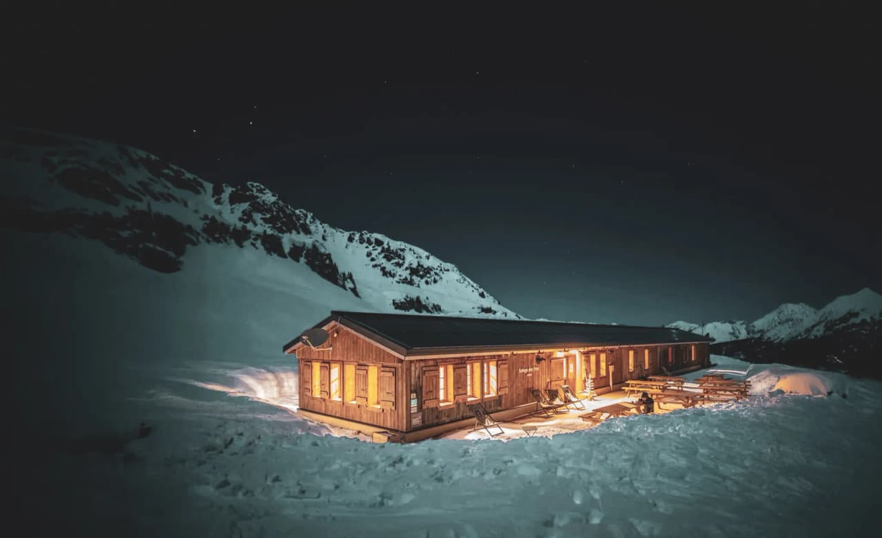 A cosy Mountain hut lit up by stars in an enchanting snowy landscape.