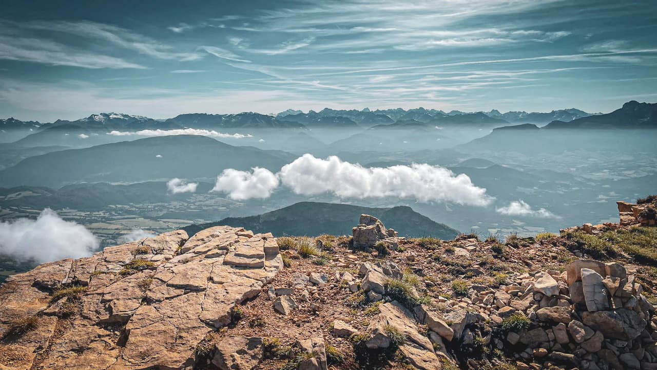 A spectacular panoramic view from the summit of Mont Aiguille, featuring mountains and clouds.