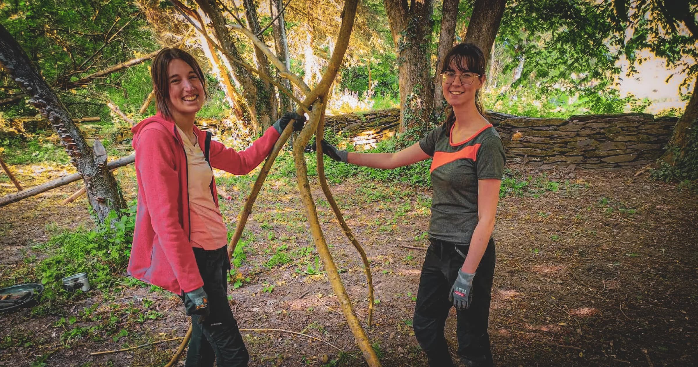 Deux participantes souriantes, réunies dans un cadre forestier verdoyant, manipulant des branches.