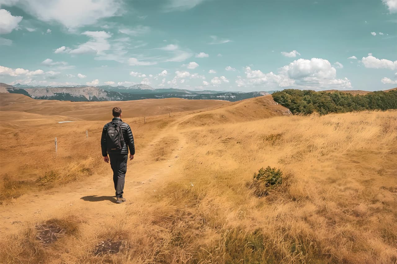Un randonneur seul traverse des paysages dorés époustouflants dans le Vercors, sous un ciel bleu.