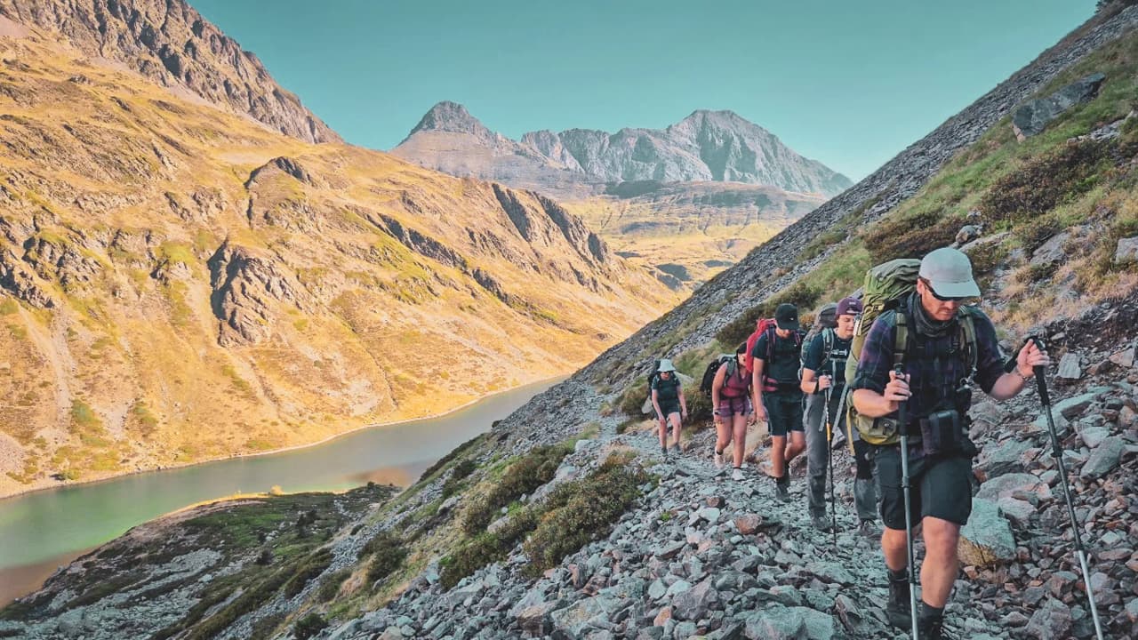 Groupe de randonneurs gravissant un sentier escarpé dans les Hautes Pyrénées, entouré de montagnes.