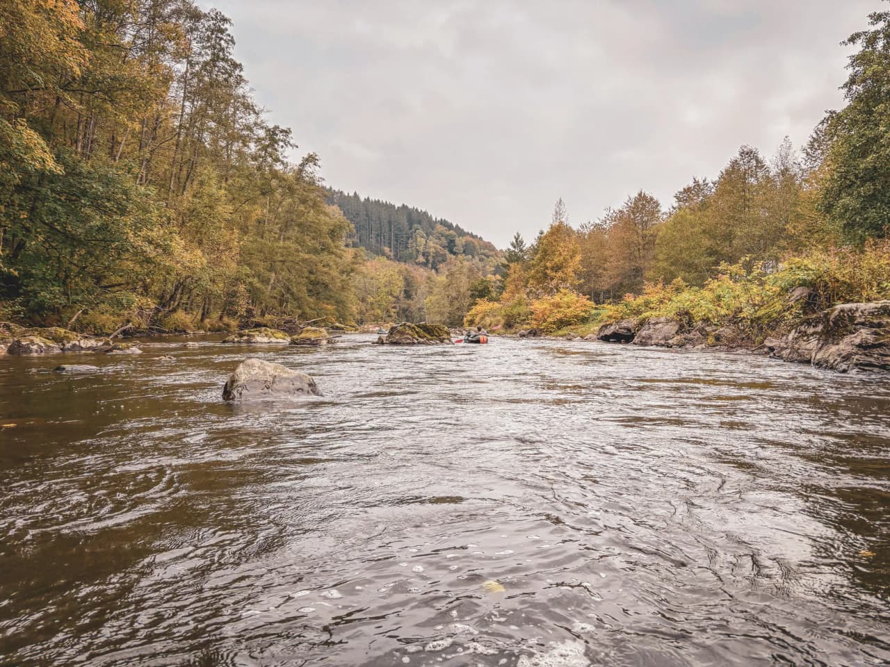Rivière tranquille en Ardenne, entourée de forêts colorées et de rochers, idéal pour l'aventure.