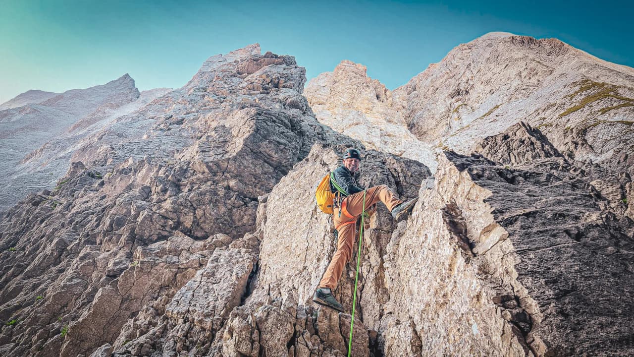 A smiling climber scales Mont Aiguille, with majestic rocks in the background.