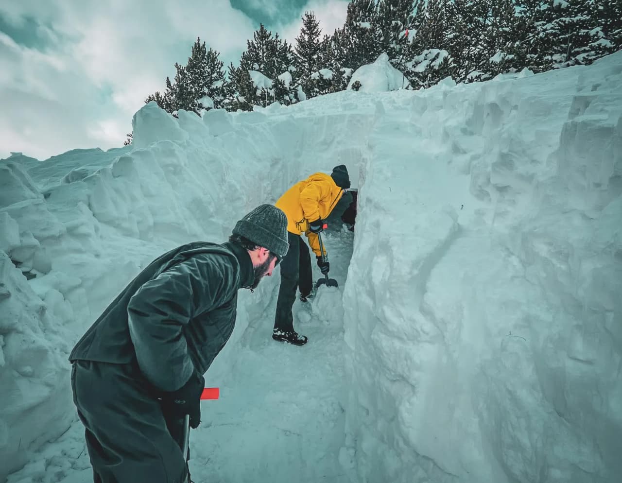 Two people dig an igloo in magnificent snow, surrounded by Alpine scenery.