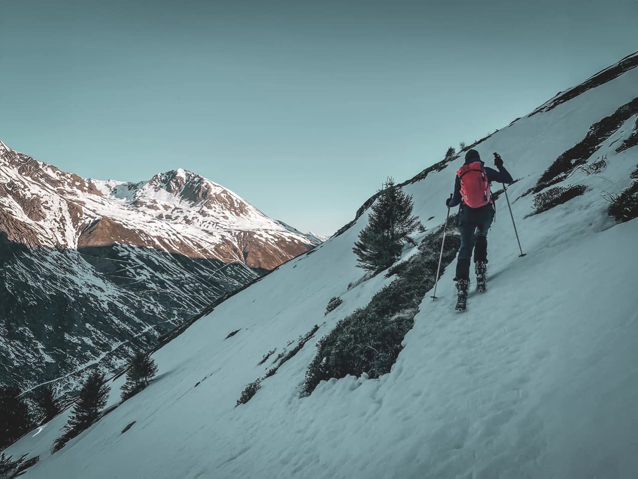 A skier follows a snow-covered trail, surrounded by majestic Alpine peaks.