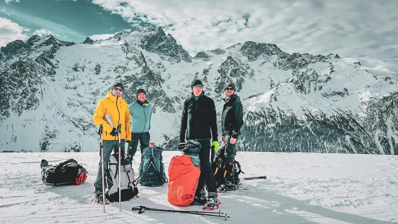 A group of hikers pose in the snow, with majestic mountains in the background.