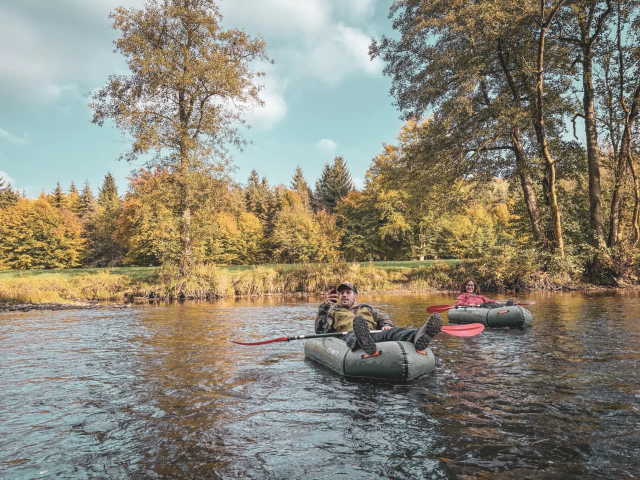 Deux personnes se détendent en packraft sur une rivière entourée de forêts aux couleurs d'automne.
