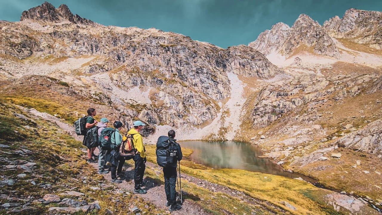 Groupe de randonneurs admirant un lac d'altitude dans les Hautes Pyrénées, paysages majestueux.