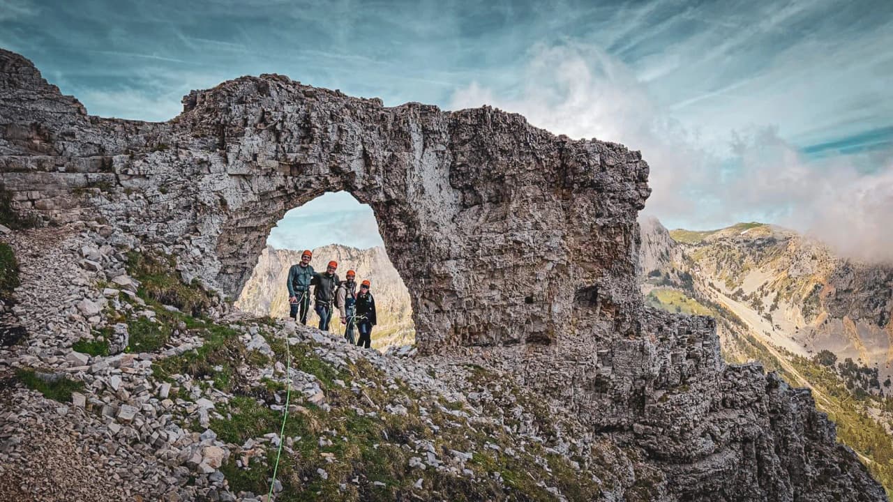 A group of climbers admiring a majestic rock arch at Mont Aiguille – a breathtaking landscape.