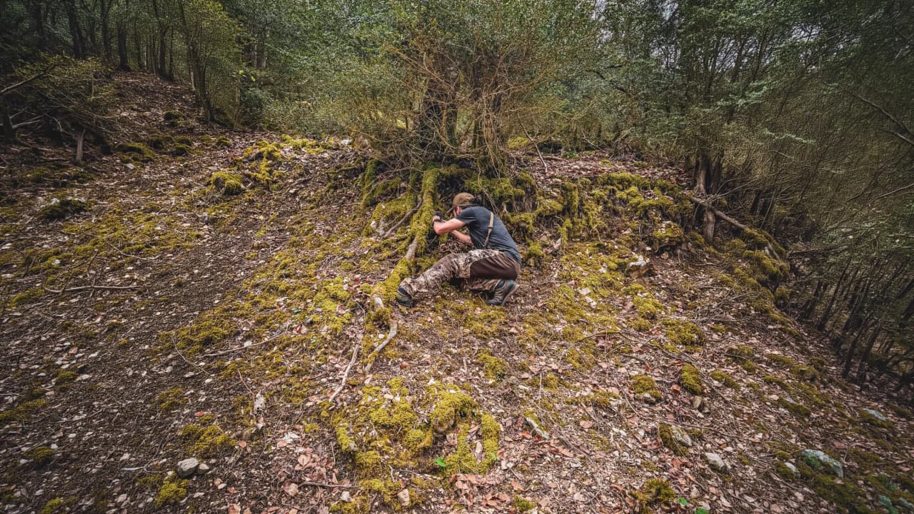 Un aventurier scrutant le sol verdoyant du Vercors, entouré de nature sauvage et préservée.