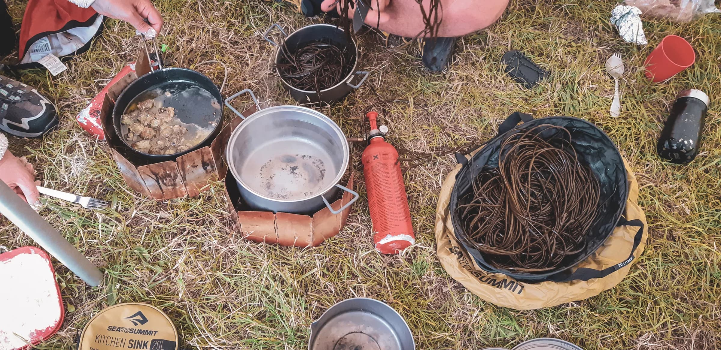 Preparing dishes in the open air, pots and ingredients in the midst of lush greenery.