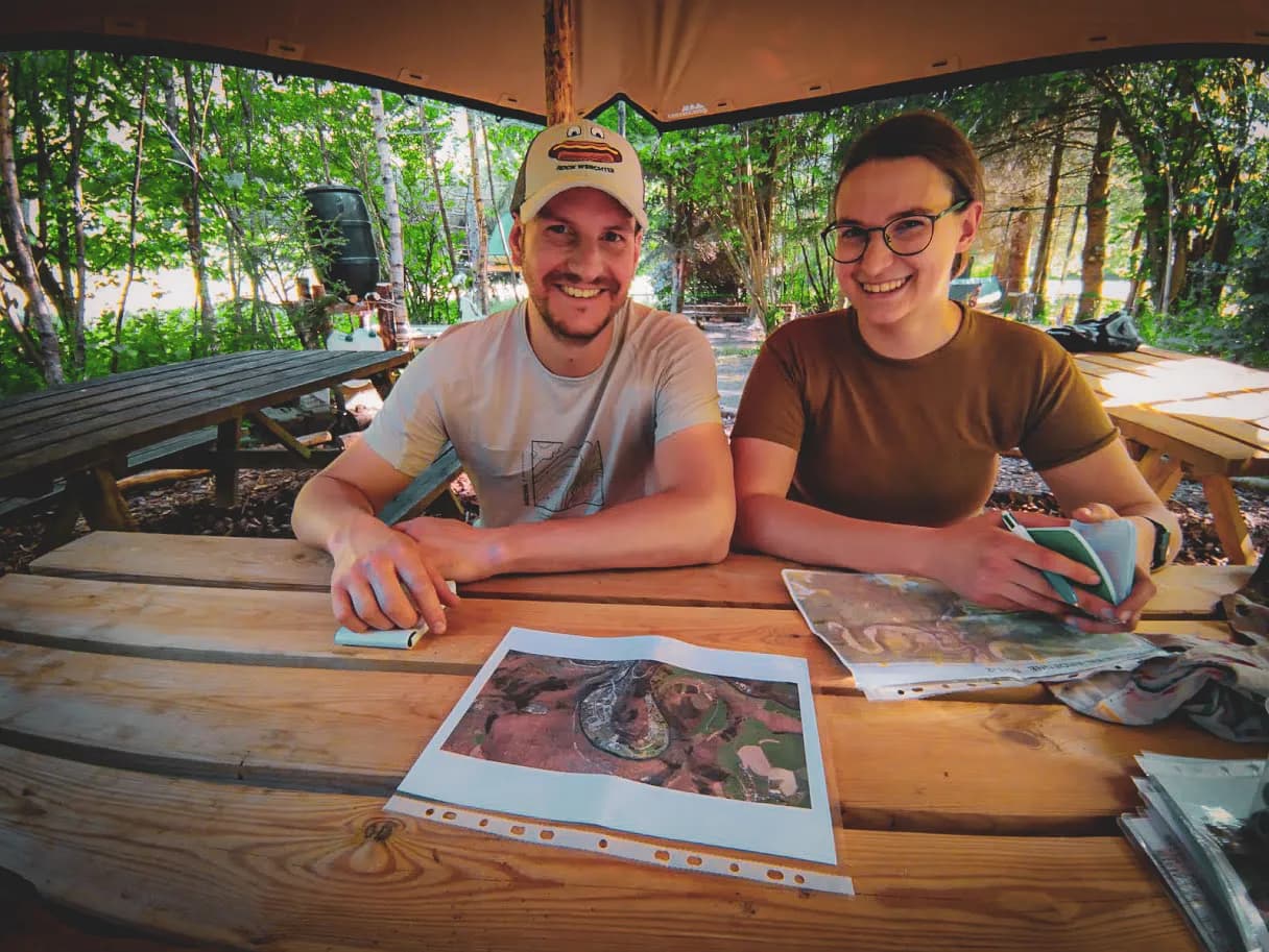 Deux personnes souriantes autour d'une table en bois, prêtes pour une aventure en forêt.